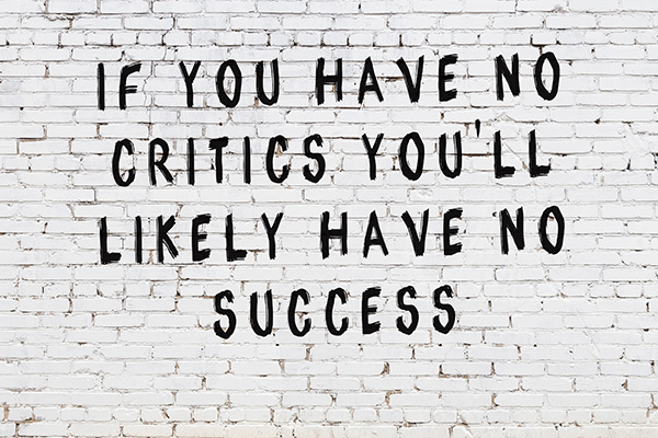 Text on a white brick wall reads, IF YOU HAVE NO CRITICS YOULL LIKELY HAVE NO SUCCESS in bold, uneven black letters